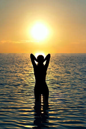 girl stands in sea water in the rays of the setting sunの写真素材