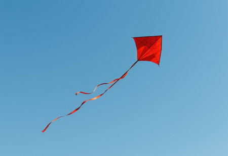 A vibrant red kite soars high in a clear blue sky its long tail streaming behind it.の素材