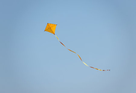 A vibrant red kite soars high in a clear blue sky its long tail streaming behind it.の素材