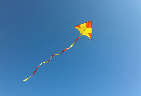 A vibrant red kite soars high in a clear blue sky its long tail streaming behind it.の素材