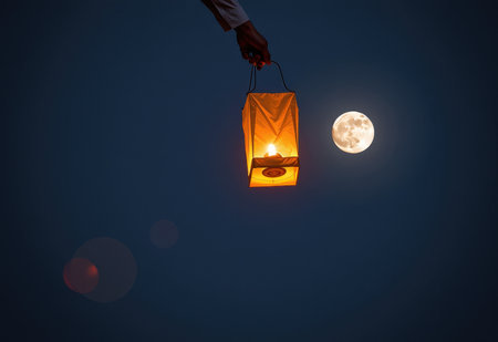 A glowing red Chinese lantern ascends into a night sky illuminated by a full moon and wispy clouds.の素材