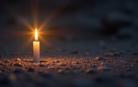 A single lit candle standing alone on the ground, casting a warm and soft glow in the darkness. This image symbolizes hope, solitude, meditation, remembrance, and spiritual connection.の素材