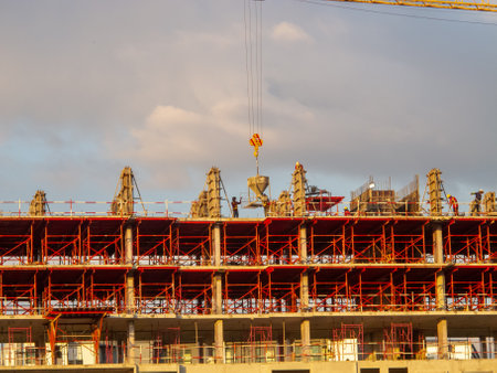 A vibrant image of a construction site during golden hour, showcasing workers engaged in concrete pouring and steel framework assembly with cranes overhead.の写真素材