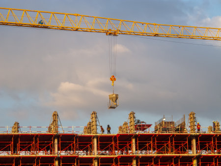 A construction site features a crane lifting materials against a backdrop of a vibrant sky. Workers collaborate on structural elements, exemplifying teamwork and industry progress.の写真素材