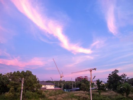 Captivating sunrise view over a construction site featuring cranes against vibrant clouds. This image captures the essence of development and nature.の写真素材
