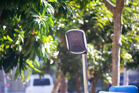 A modern parking meter stands under the bright sunlight, surrounded by lush greenery, showcasing urban infrastructure and payment technology in a city environment.の写真素材