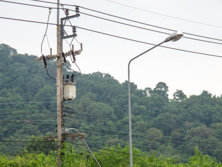 A utility pole stands with power lines against a backdrop of lush green mountains. This image captures the essence of rural electricity infrastructure.の写真素材