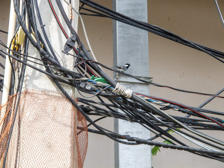A close-up view of a utility pole showcasing a jumble of electrical wires and cables. A small bird rests on the wires, blending urban infrastructure with nature.の写真素材