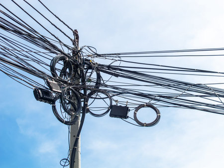 An intricate arrangement of overhead power lines and cables on a utility pole, set against a clear...