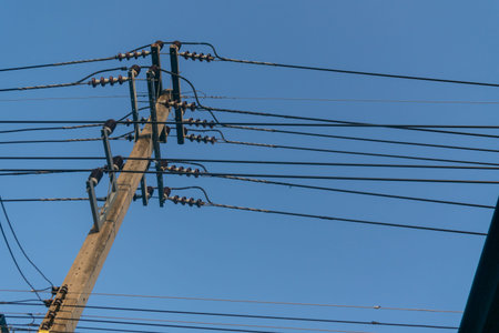 A clear view of power lines stretching across a bright blue sky. This image showcases urban...
