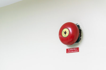 A bright red alarm bell is mounted on a plain wall, accompanied by a clear signage, highlighting its importance for safety and emergency notifications.の写真素材