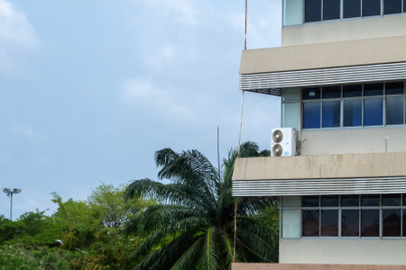 This image features a modern building equipped with an air conditioning unit alongside lush tropical vegetation, capturing urban living with comfort and nature.の写真素材
