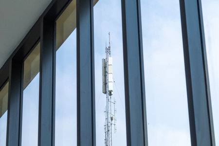 A sleek communication tower stands tall, beautifully reflected in modern building windows, showcasing the intersection of technology and urban design in a vibrant cityscape.の写真素材