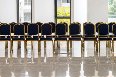 A row of neatly arranged chairs in a modern event space showcases a bright and inviting atmosphere, ideal for meetings or gatherings. The reflective floor adds elegance.の写真素材