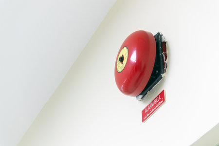 A bright red fire alarm bell mounted prominently on a white wall, symbolizing safety and emergency readiness in urban buildings. The device highlights the importance of alertness and readiness.の写真素材
