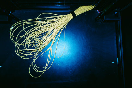 A vivid bundle of yellow wires lies on a black surface, illuminated by low light. This image...