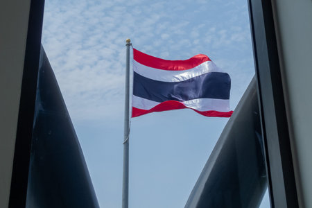 A vibrant flag of Thailand waves gracefully against a clear blue sky. The scene captures the essence...