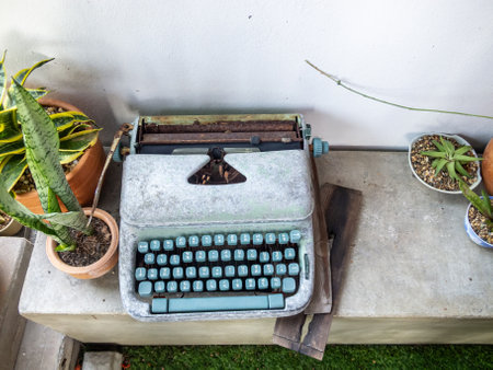 A vintage typewriter placed on a wooden surface, surrounded by lush green plants, creates a cozy and inspirational workspace ambiance. Perfect for writing enthusiasts.の写真素材