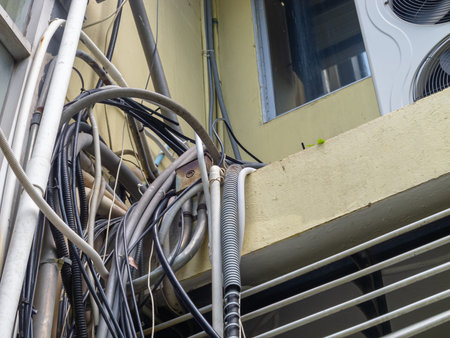 A close-up view of tangled electrical wires and pipes against a building's exterior. The intricate...