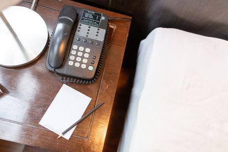 A close-up view of a desk phone beside a notepad and pen on a wooden table. Ideal for showcasing hospitality, communication, or office settings.の写真素材