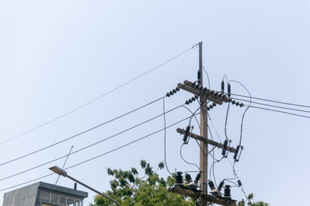 A clear view of power lines and poles against a blue sky in an urban setting. The intricate wiring and structures display the essential role of electricity in modern life.の写真素材