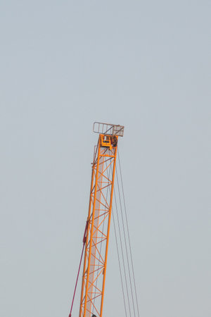 A tall orange crane stands prominently against a clear blue sky, symbolizing industrial progress and construction activities. This image captures the essence of modern engineering.の写真素材