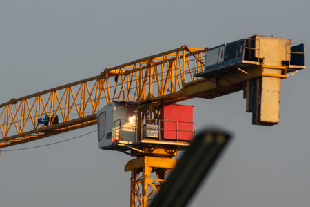 A detailed view of a construction crane operating at a building site, showcasing its yellow arm,...