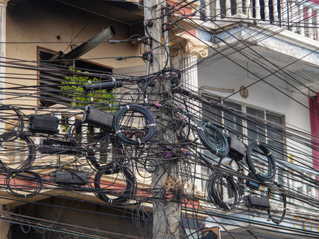 An intricate web of electrical wires and cables crisscrosses an urban environment, showcasing the...