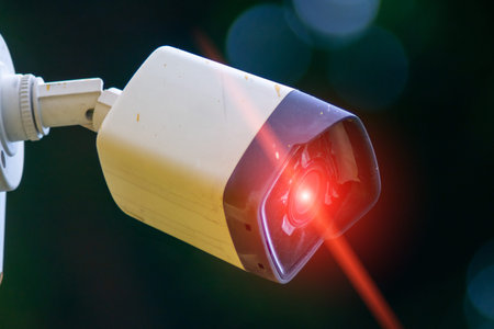 A close-up of a security camera featuring a red light, set against a blurred background. This image...