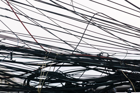 A complex arrangement of tangled wires and cables creates an intricate pattern against a gray sky. This urban scene captures the chaos of modern infrastructure.の写真素材