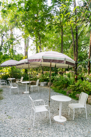 A peaceful outdoor dining area featuring white furniture and striped umbrellas, set against a lush green backdrop, ideal for relaxation and gatherings.の写真素材