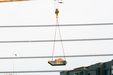 A crane lifts construction material high above buildings, showcasing urban development. This image highlights industry dynamics and modern architecture in action.の写真素材