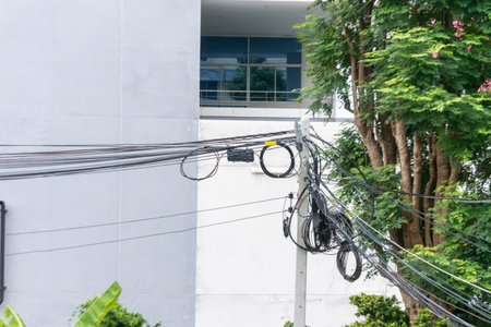 A detailed view of power lines and cables intertwining against an urban building backdrop, showcasing modern infrastructure and city life intersection.の写真素材