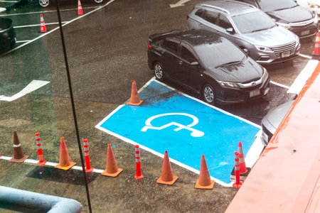 This image shows an accessible parking space marked in blue, surrounded by safety cones in rainy weather. The scene emphasizes urban infrastructure and accessibility awareness.の写真素材