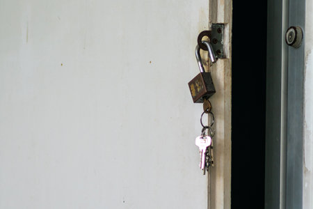 A close-up image of a padlock securing a door, with keys hanging nearby. The door's texture highlights a sense of safety and accessibility. Perfect for themes of security and home.の写真素材