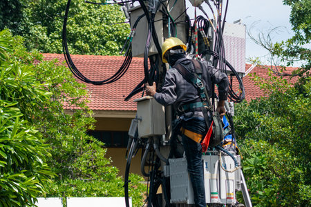 A technician climbs an electric utility pole to perform maintenance work. Safety gear is essential in this critical task amidst greenery and infrastructure.の写真素材