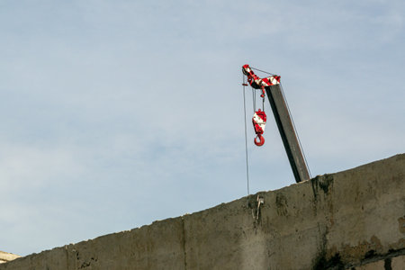 A construction crane stands over a building site, showcasing industrial work in an urban environment. The bright red colors contrast against a clear sky.の写真素材