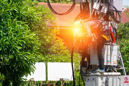A technician performs maintenance on electrical equipment at a height, showcasing safety practices and tools in a bright outdoor setting.の写真素材