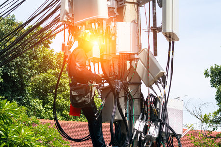 A technician performs maintenance on a telecom tower, showcasing the intricate network of cables and technology needed for modern communication infrastructure.の写真素材