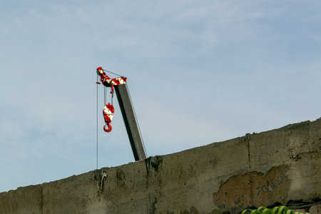 A construction site scene featuring a crane with a red hook against a blue sky, highlighting urban development and industrial activity involved in building projects.の写真素材