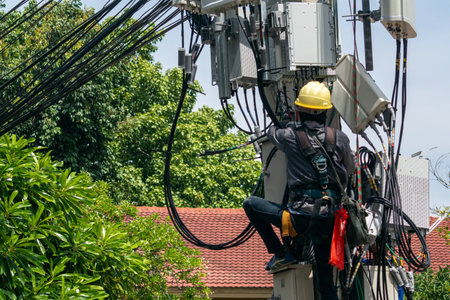 A technician safely climbs an electric pole to perform maintenance on communication cables and infrastructure in an urban environment.の写真素材