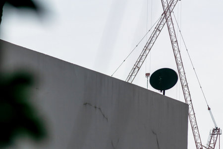 A close-up view of a construction site featuring a tall crane, mounted equipment, and a stark wall, highlighting urban development and industrial activity.の写真素材