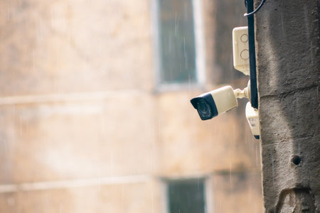A detailed view of a CCTV camera mounted on a utility pole during rainfall, emphasizing urban security and technology in a rainy street environment.の写真素材