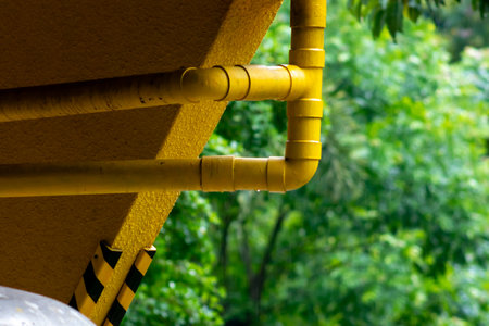 A close-up image of a yellow pipe stretching against a lush green background, showcasing the contrast between urban infrastructure and nature.の写真素材
