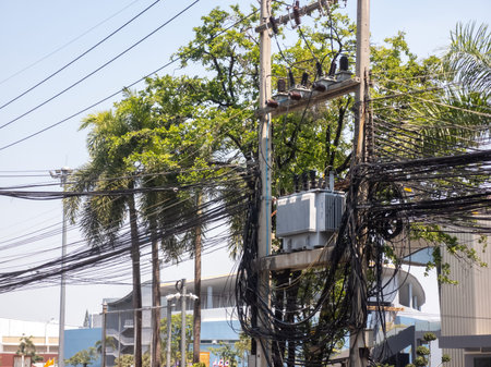 A detailed view of power lines and a transformer surrounded by green trees in an urban setting,...
