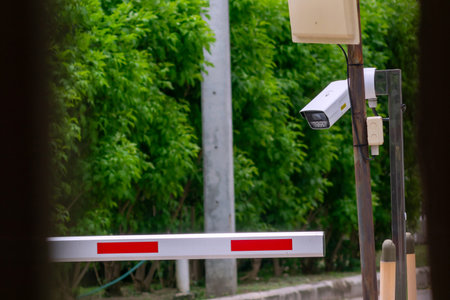 A surveillance camera positioned strategically at a gate entrance, equipped for monitoring and security purposes. Lush green background contrasts with the technology.の写真素材