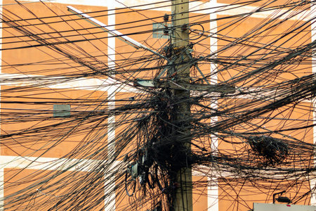 An intricate display of tangled overhead wires on a utility pole, highlighting urban infrastructure and the complexity of electric and telecommunication systems.の写真素材