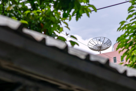 A satellite dish perched on a rooftop surrounded by lush greenery. The image captures the blend of technology and nature in an urban setting.の写真素材