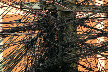 This image features a chaotic arrangement of wires and cables on a utility pole against an orange background, highlighting urban infrastructure and connectivity.の写真素材