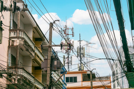 A vibrant urban scene featuring communication towers amid buildings and power lines, showcasing the intersection of technology and city life under a bright blue sky.の写真素材
